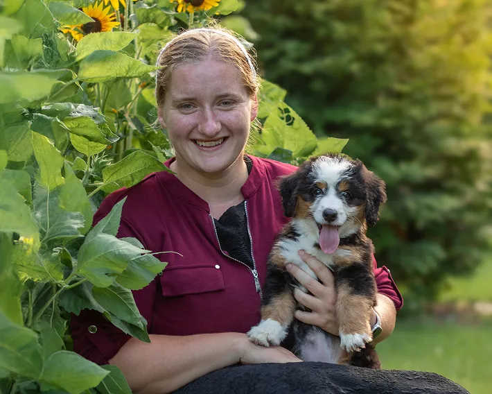 Ruby Miller holding an adorable puppy in a field of sunflowers.