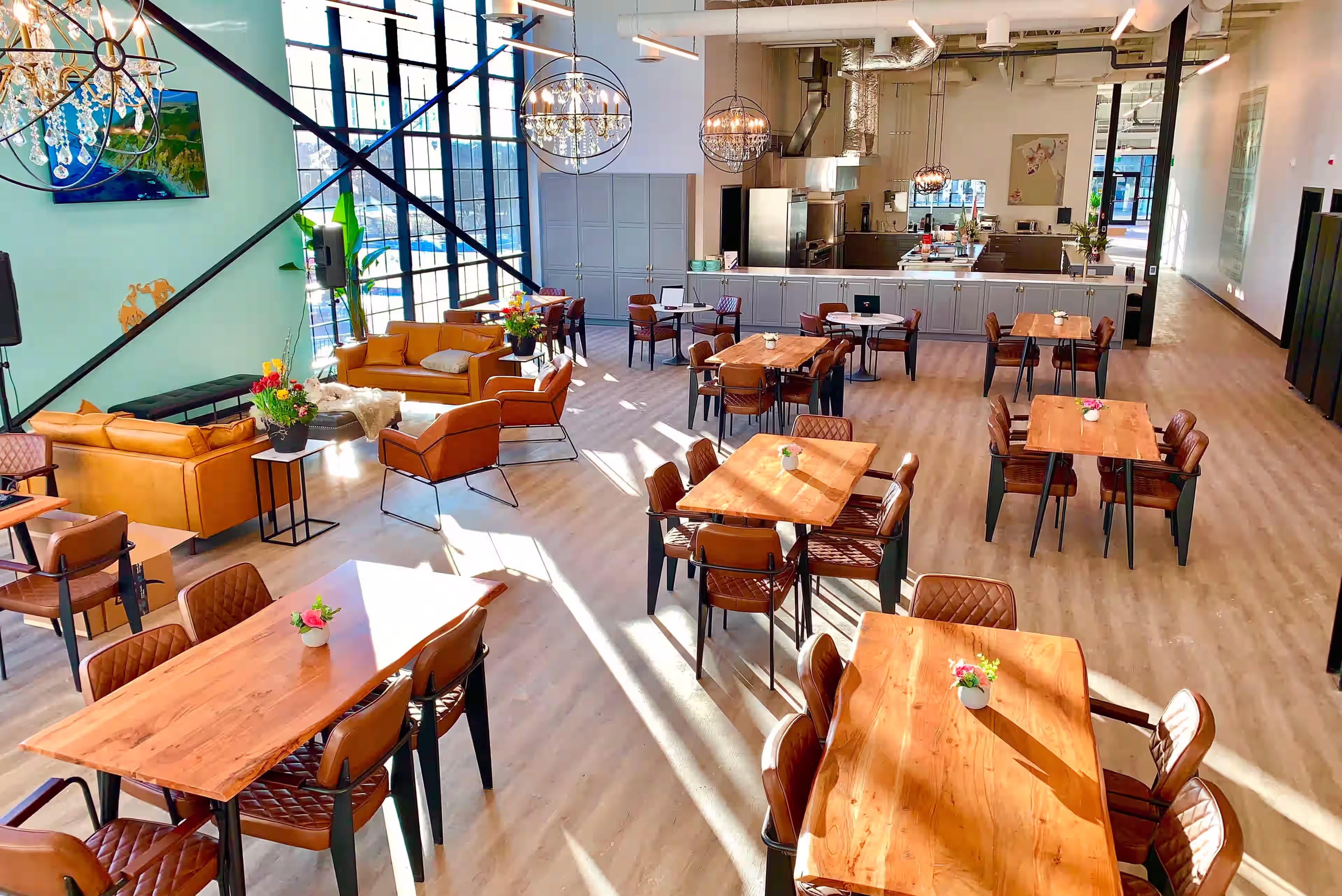 A bright, modern dining area with tall windows, wooden tables, and a turquoise accent wall. The open kitchen lets residents enjoy tea or a light snack in a stylish, minimalist setting.