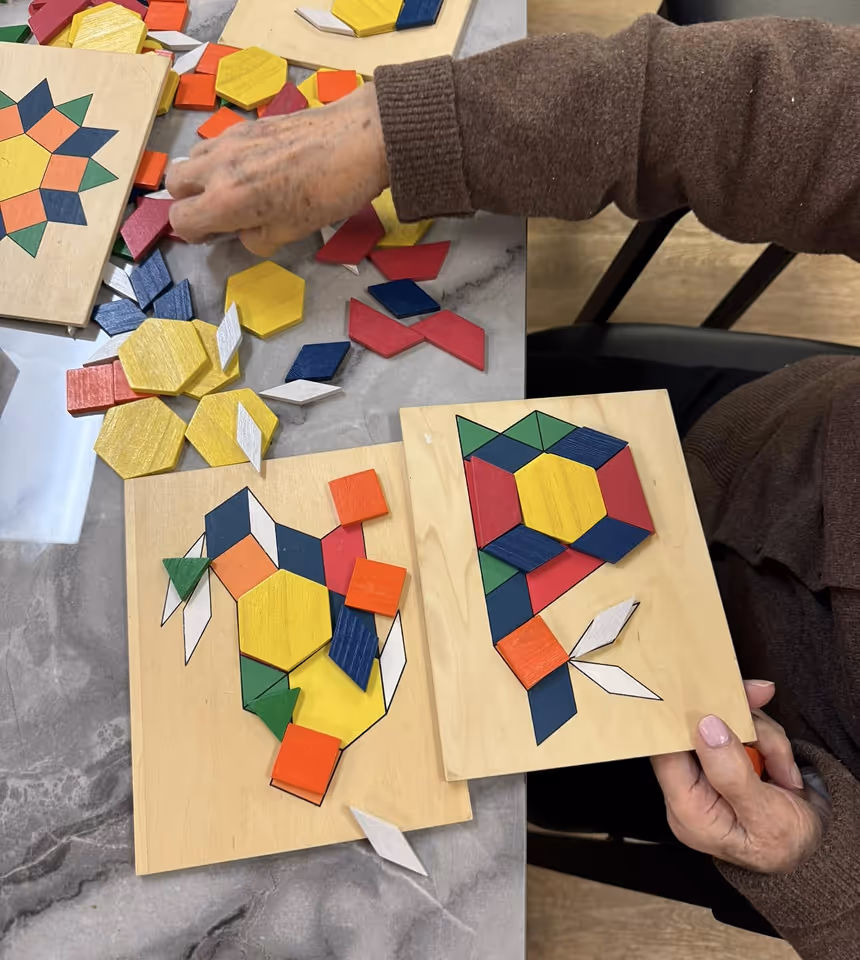 An older adult arranges wooden geometric pieces on a board, matching shapes to form an animal pattern.