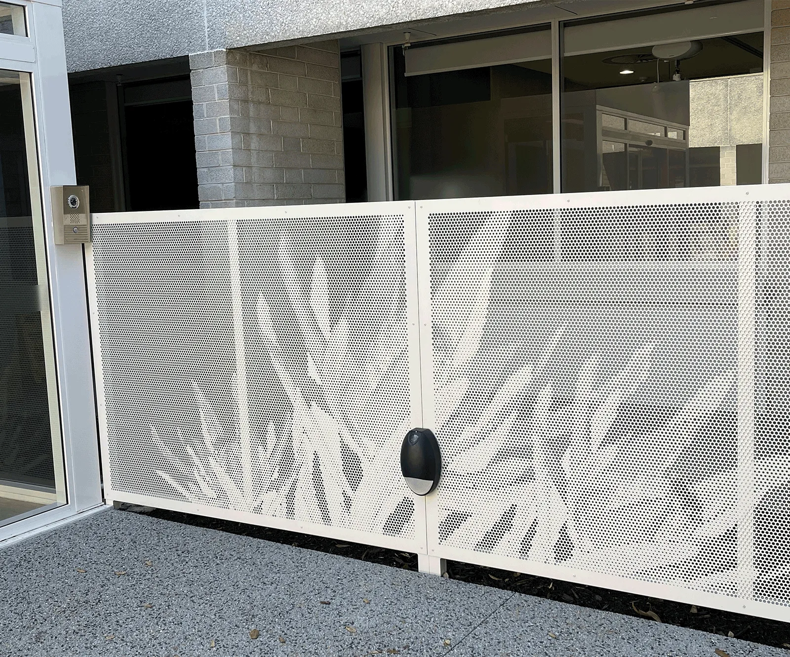 White perforated metal fence panel with cutout design of large abstract leaves in front of a building entrance.