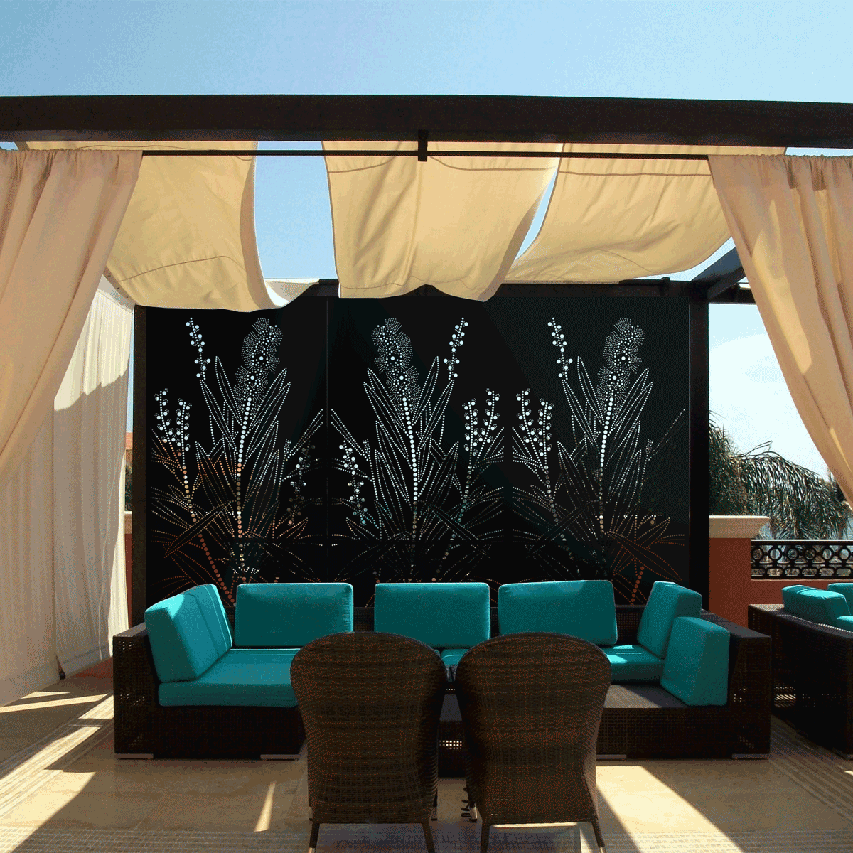Outdoor patio seating area with turquoise cushions, wicker chairs, and decorative black privacy screens with a botanical pattern under beige fabric canopy.