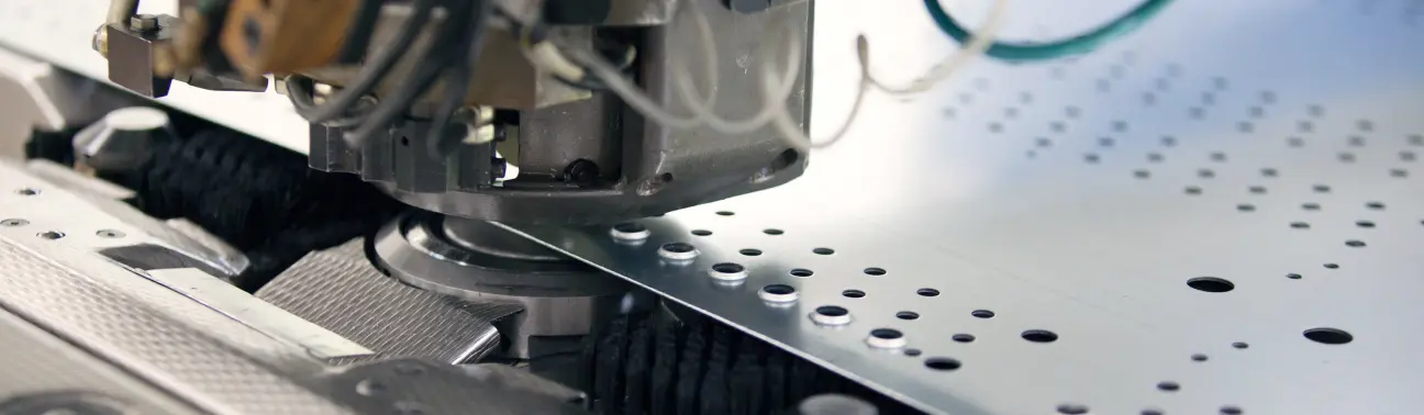 Close-up of a turret punch machine working on a metal sheet with multiple punched holes.
