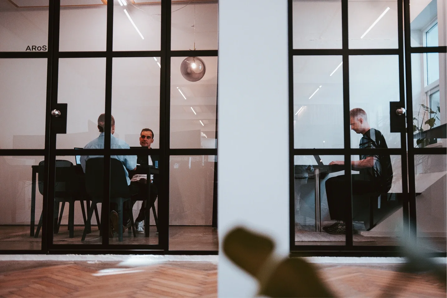 Kontor stills af Better Developers. Der ses to mødelokaler, hvori der er et møde i det ene og i det andet lokale sidder vores udvikler Thomas og arbejder