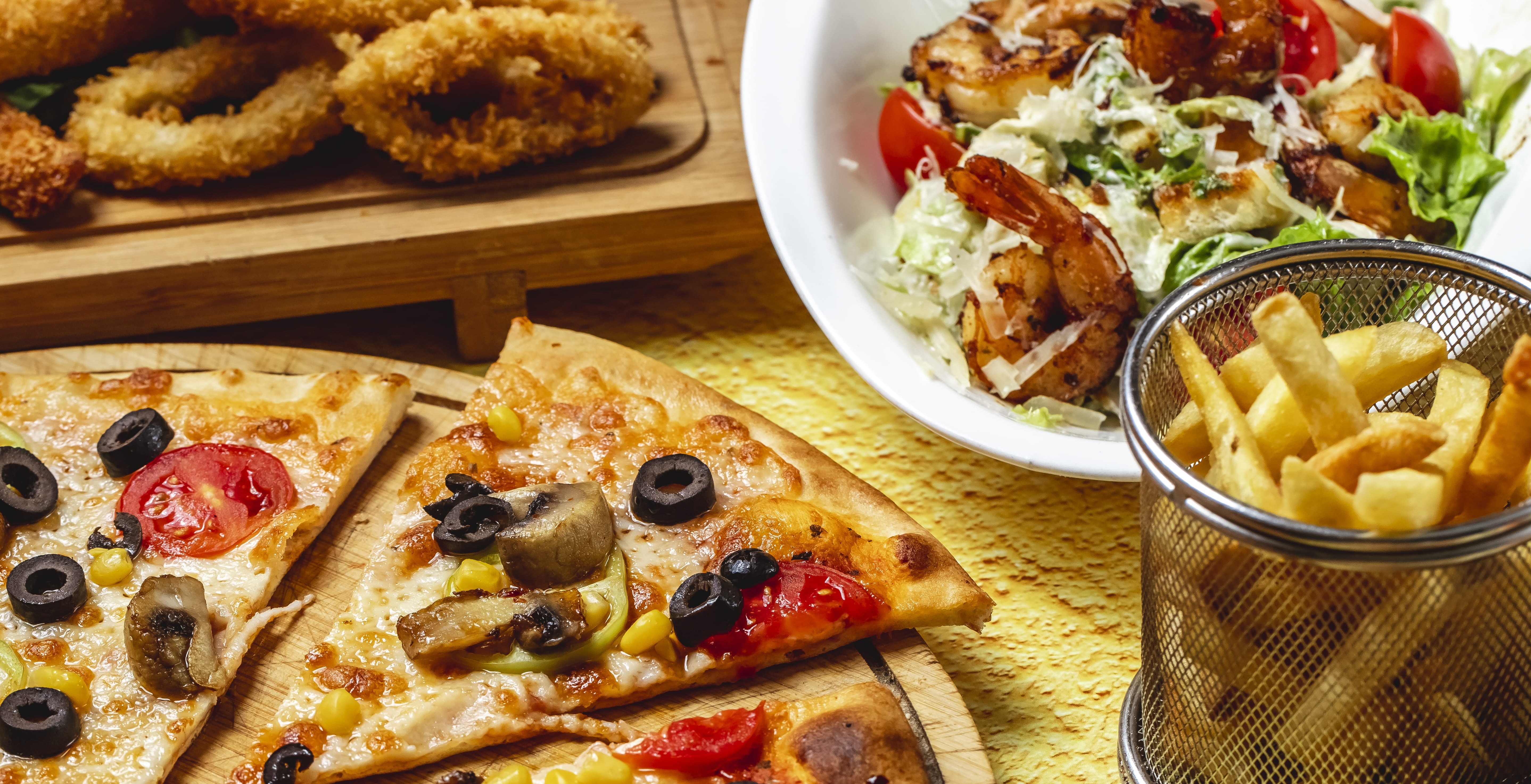 una mesa con pizza papas fritas y ensalada