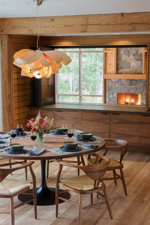 Round dining table and mid century chairs over looking screen porch with fire in the fireplace.