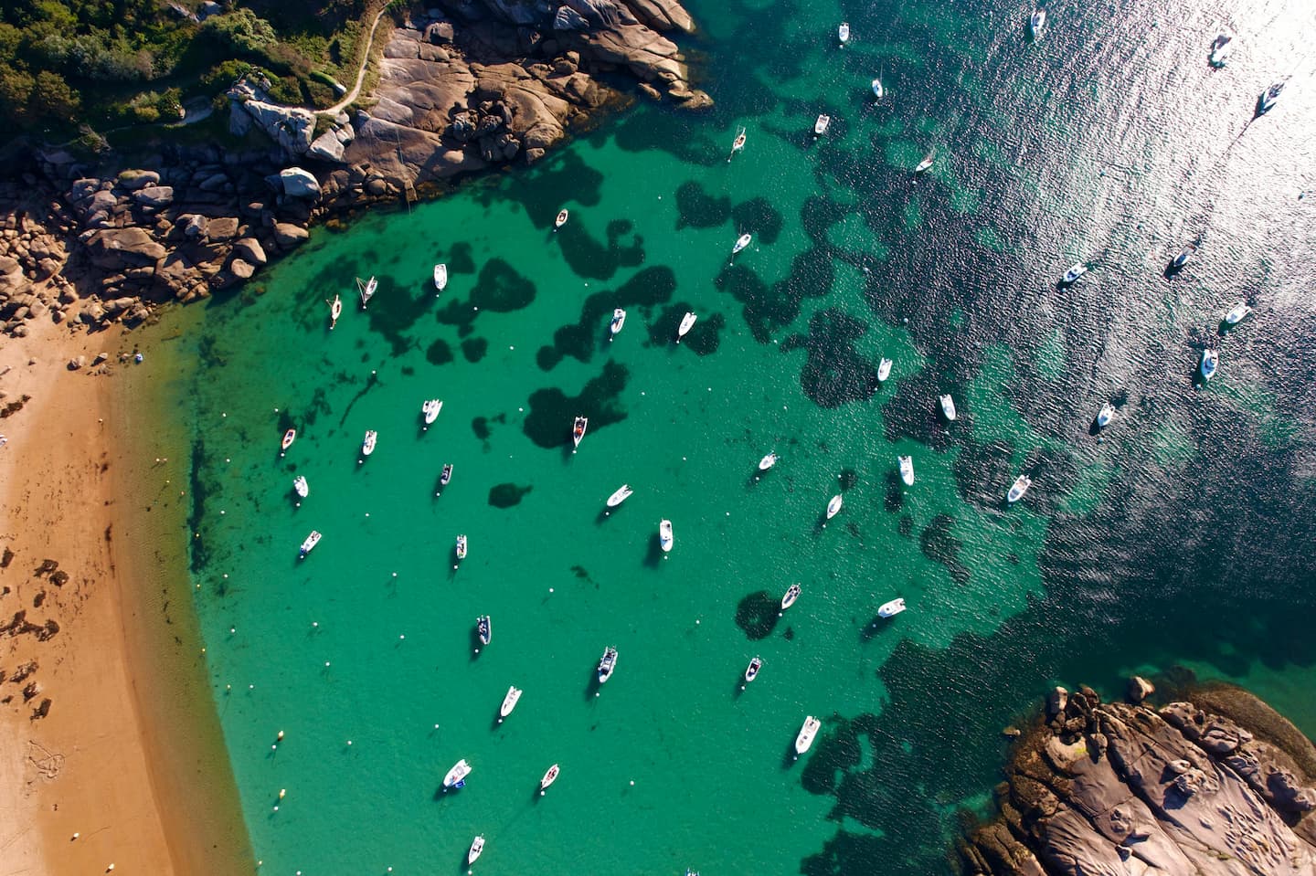 Vue aérienne d’une crique bretonne aux eaux turquoise, parsemée de bateaux de plaisance — invitation à l’évasion offerte par la carte cadeau Bretagne Emotion