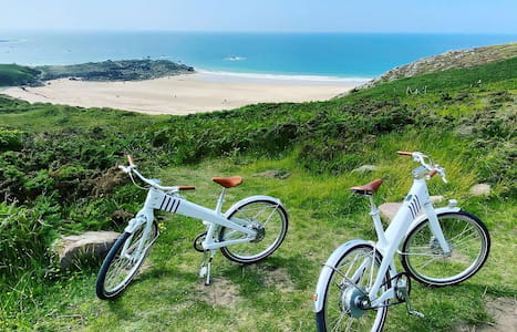 Deux vélos blancs stationnés sur une colline verdoyante avec vue panoramique sur la plage et l’océan en Bretagne