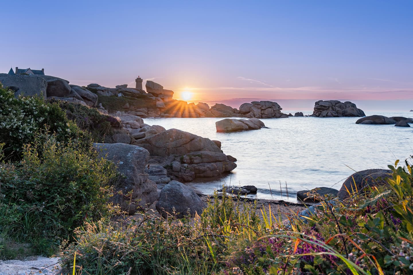 Coucher de soleil sur la côte de granit rose en Bretagne, avec vue sur un phare et les rochers sculptés par la mer.
