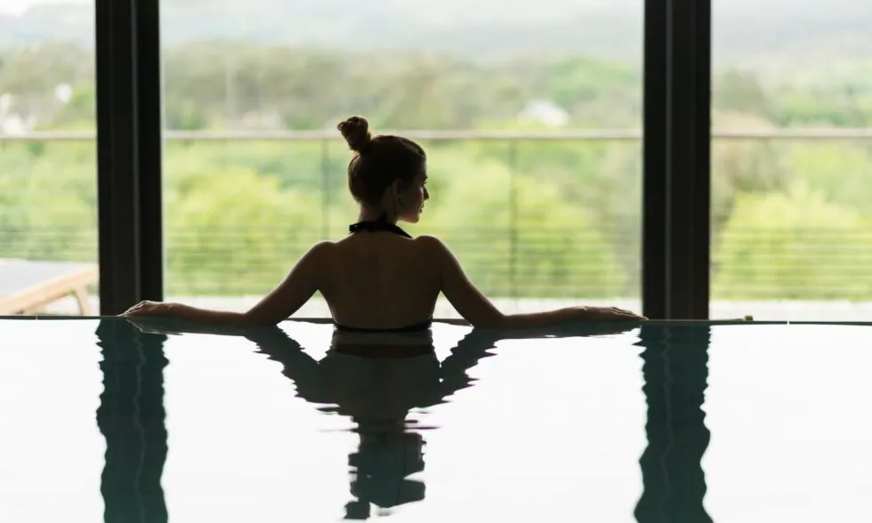Femme profitant d’un moment de détente dans la piscine intérieure du spa de l’hôtel La Grée des Landes, avec vue sur la nature du Morbihan