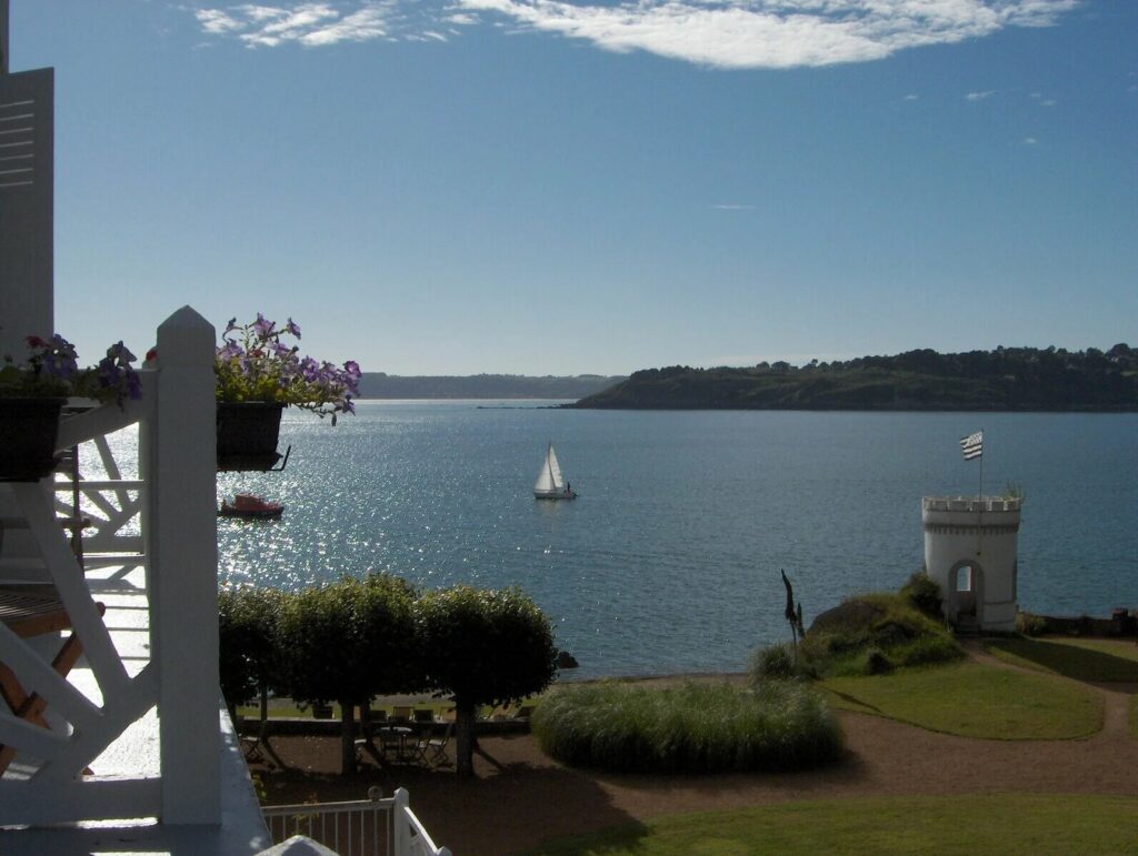 View of the sea and the Brittany coast from the Grand Hôtel des Bains in Locquirec, with a sailboat and a turret by the sea.