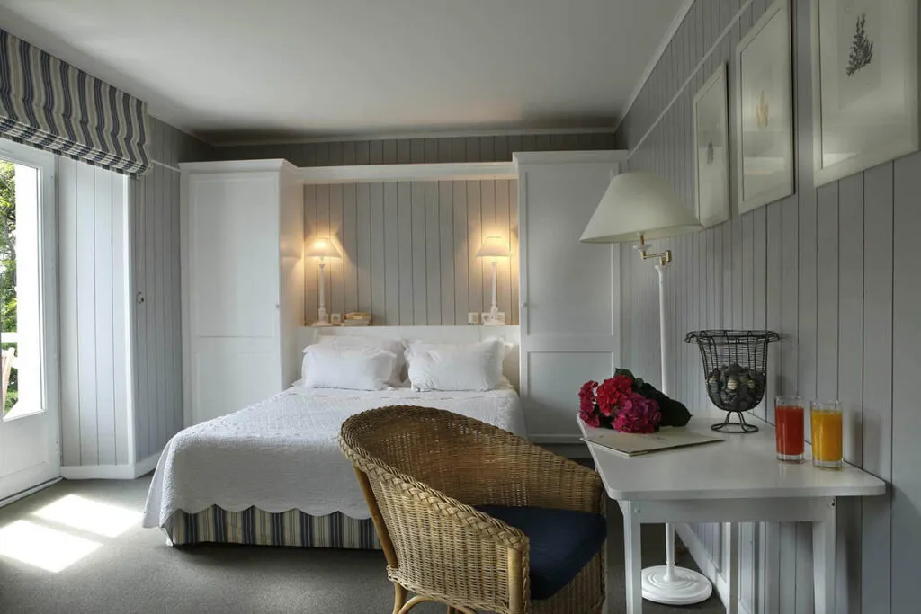 Chambre lumineuse au style Nouvelle-Angleterre avec murs en bois gris, lit double et mobilier blanc dans un hôtel de charme du Finistère