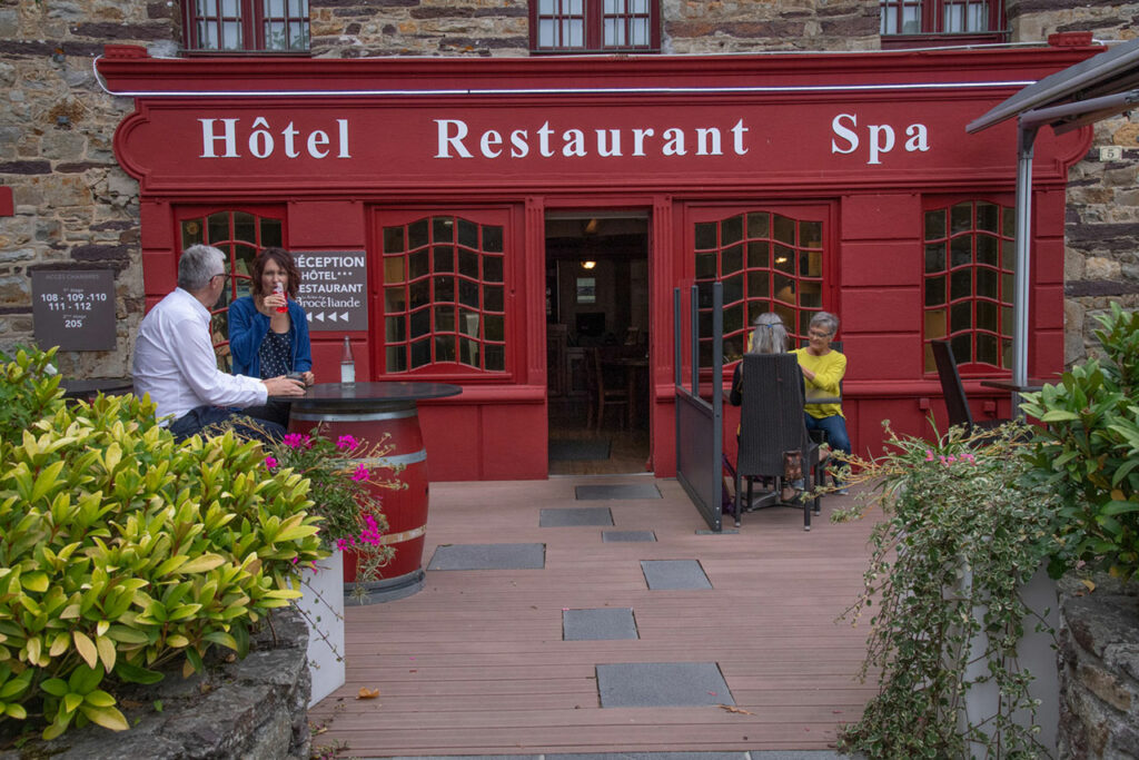 Stone facade and red sign at the Relais de Brocéliande in Paimpont, with the hotel restaurant spa's convivial terrace.