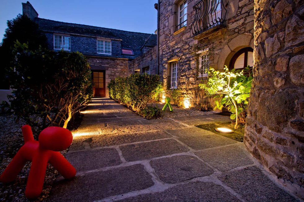 Entrée éclairée de l’hôtel Le Temps de Vivre à Roscoff en soirée, avec façade en pierre et décoration design
