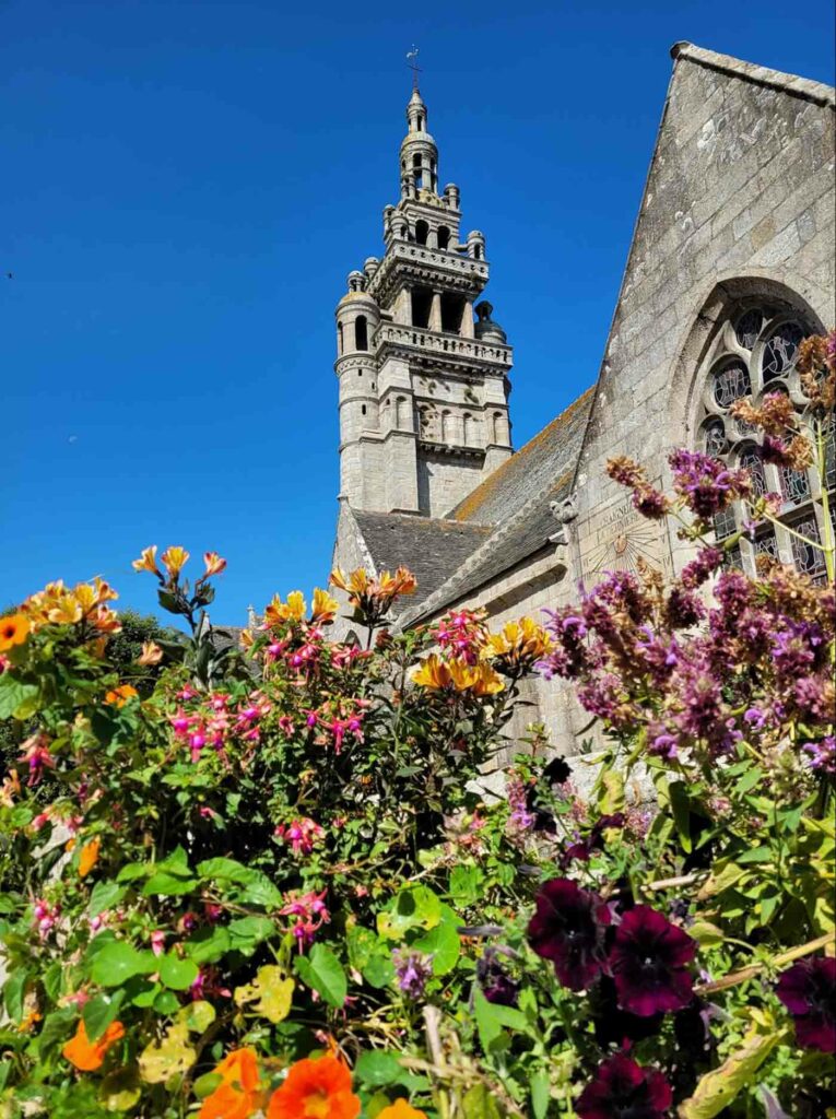 Église de Roscoff vue depuis un parterre fleuri, sous un ciel bleu éclatant
