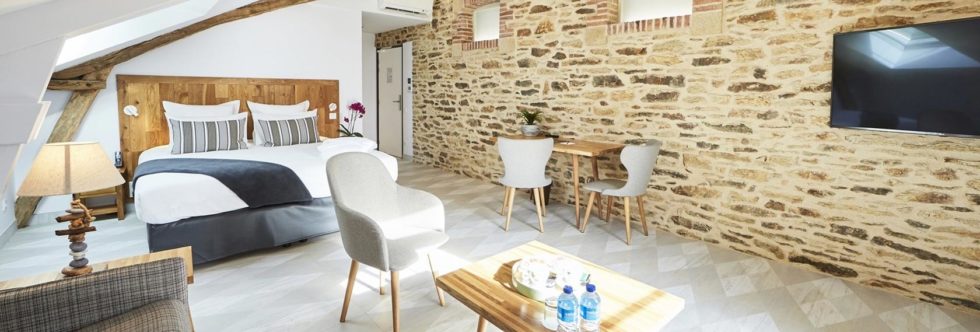 Spacious, bright room with exposed stone walls, double bed, sitting area and TV, in a seaside hotel