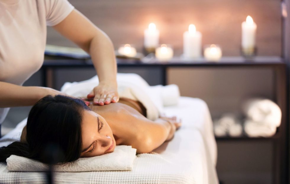 Woman receiving a relaxing massage in a hotel spa, dimmed atmosphere with candles lit in the background.