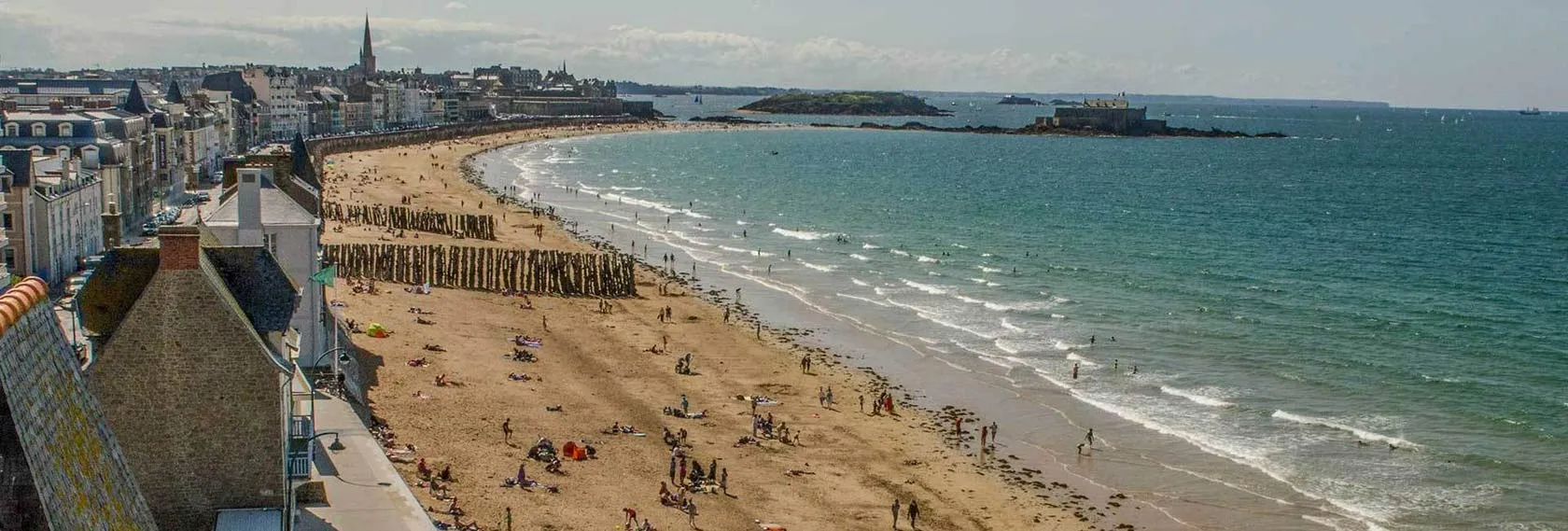 Vue panoramique sur la grande plage de Saint-Malo avec ses remparts, ses brise-lames et l’océan à perte de vue.