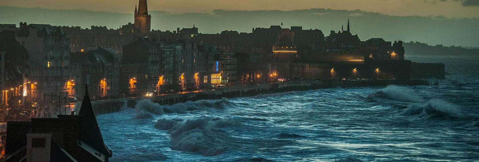 Night view of the Intra-Muros ramparts in Saint-Malo, with rough seas and waves hitting the seawall.