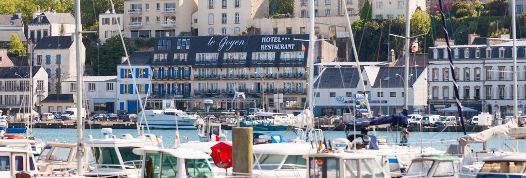Vue sur l’Hôtel Le Goyen à Audierne, en bordure du port de plaisance, entouré de bateaux et de maisons typiques bretonnes.