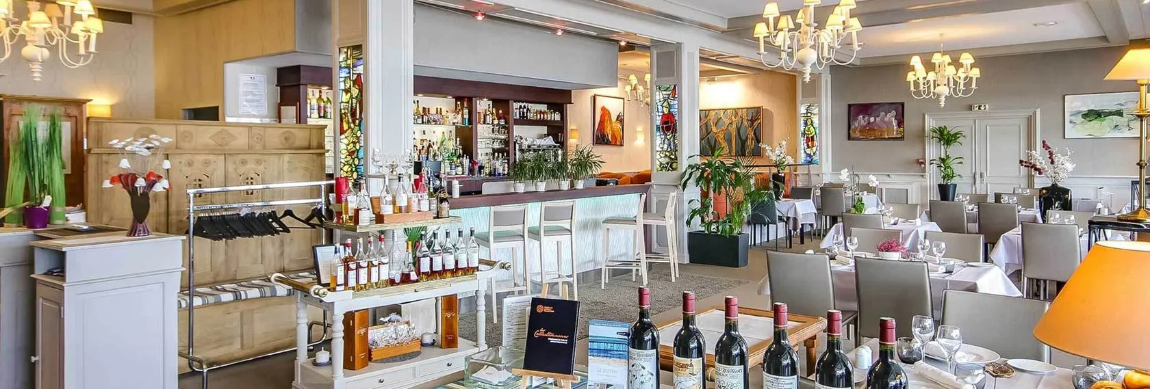 Salle du restaurant gastronomique de l’Hôtel Le Goyen, élégamment décorée avec chandeliers, œuvres d’art, et sélection de vins, invitant à une expérience culinaire raffinée.