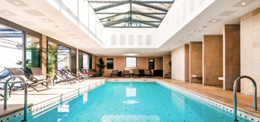 Piscine intérieure baignée de lumière naturelle avec transats, idéale pour se détendre après une randonnée sur le sentier des douaniers.