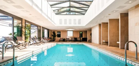 Piscine intérieure baignée de lumière naturelle avec transats, idéale pour se détendre après une randonnée sur le sentier des douaniers.