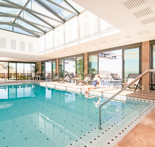 Femme assise au bord d’une piscine intérieure lumineuse à L’Agapa, symbole de détente et de luxe pour un séjour d’exception en Bretagne.