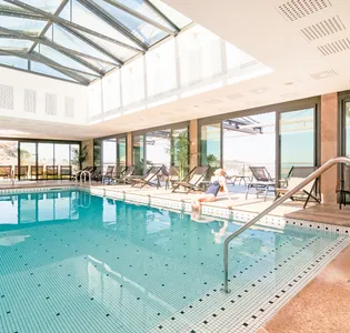 Femme assise au bord d’une piscine intérieure lumineuse à L’Agapa, symbole de détente et de luxe pour un séjour d’exception en Bretagne.