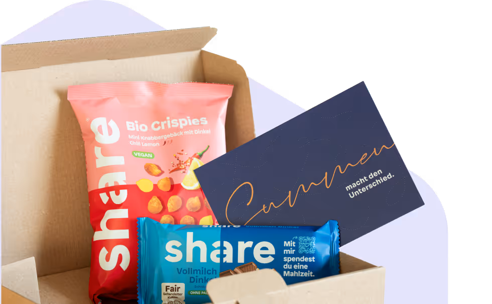 Geöffnete Schachtel mit pinkem Bio-Crispies Snack, blauem Schokoladenriegel und einer dunkelblauen Karte mit goldener Schrift.