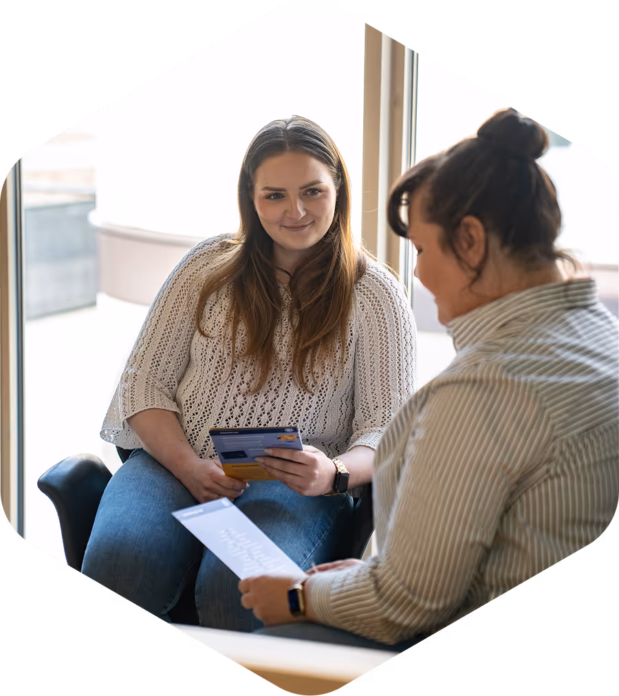 Zwei Frauen sitzen und lesen gemeinsam Informationsbroschüren in einem hellen Raum.