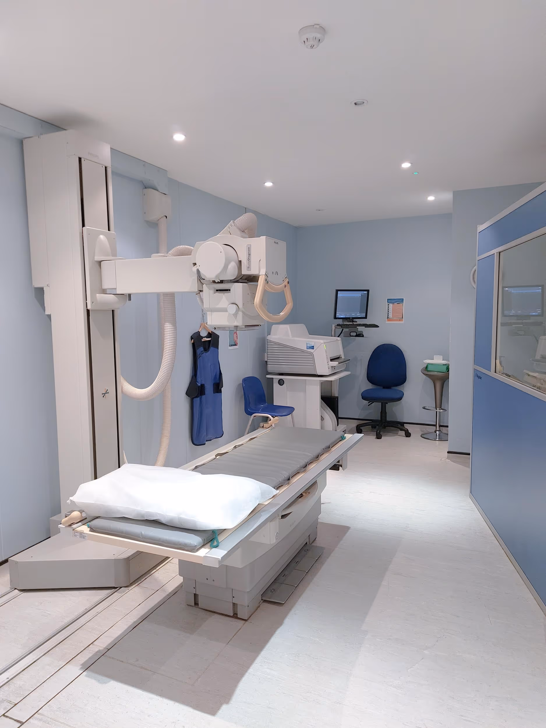 An empty X-ray room with a machine, an exam table, and a computer station.