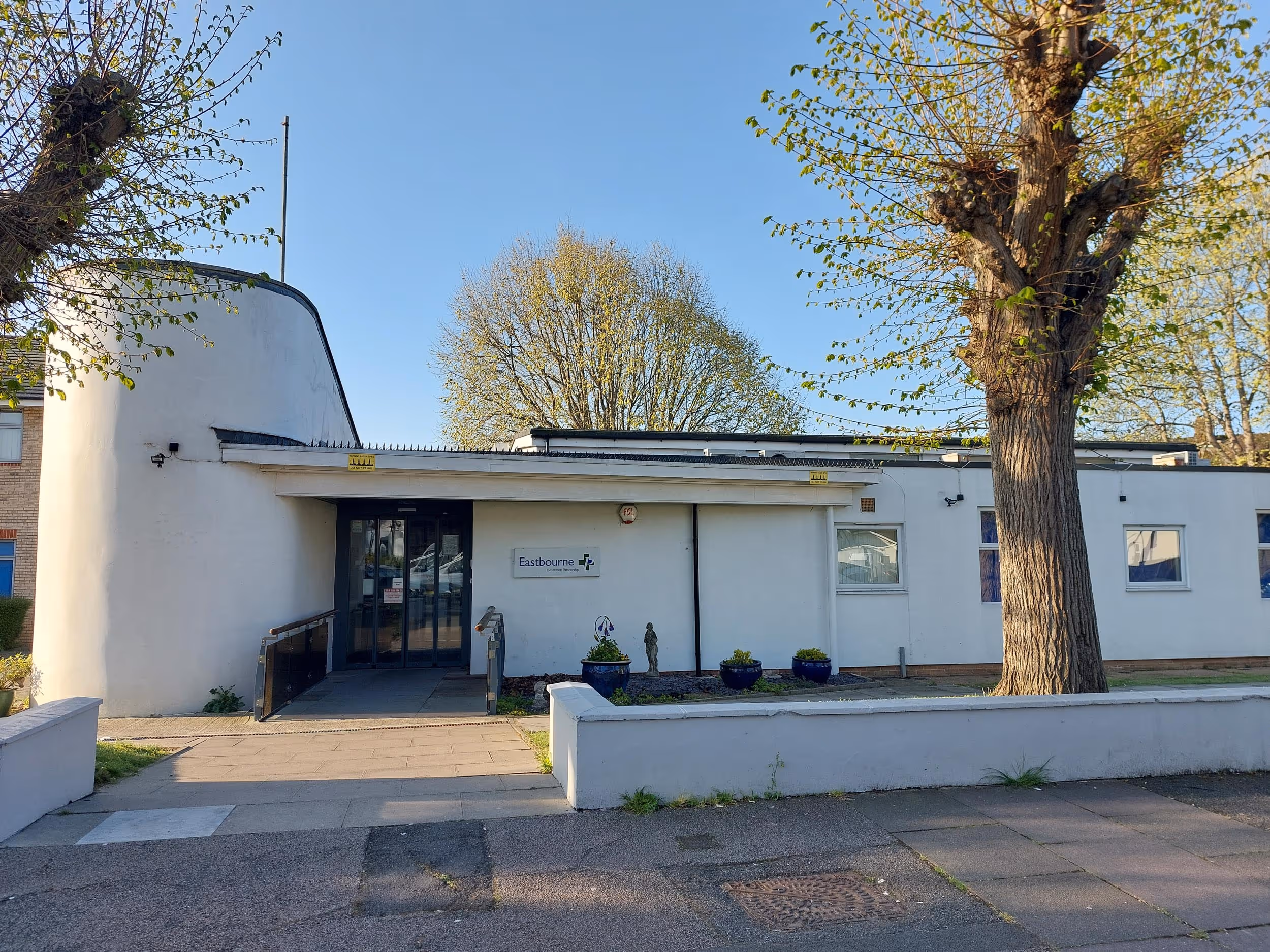 A modern white building with a glass entrance and trees on either side.