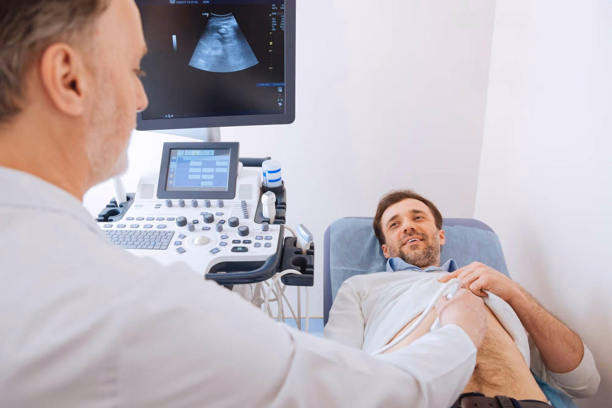 A doctor performs an ultrasound on a male patient lying on an examination table.