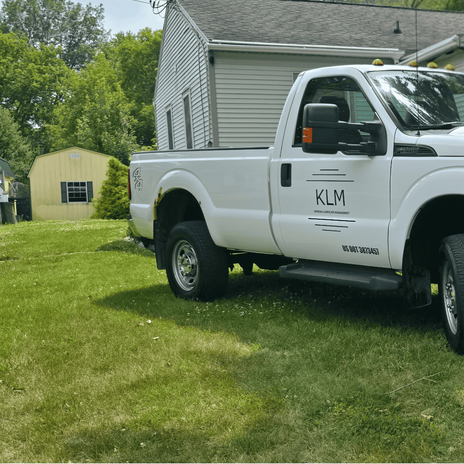 KLM Landscaping branded work truck parked on a green residential lawn.