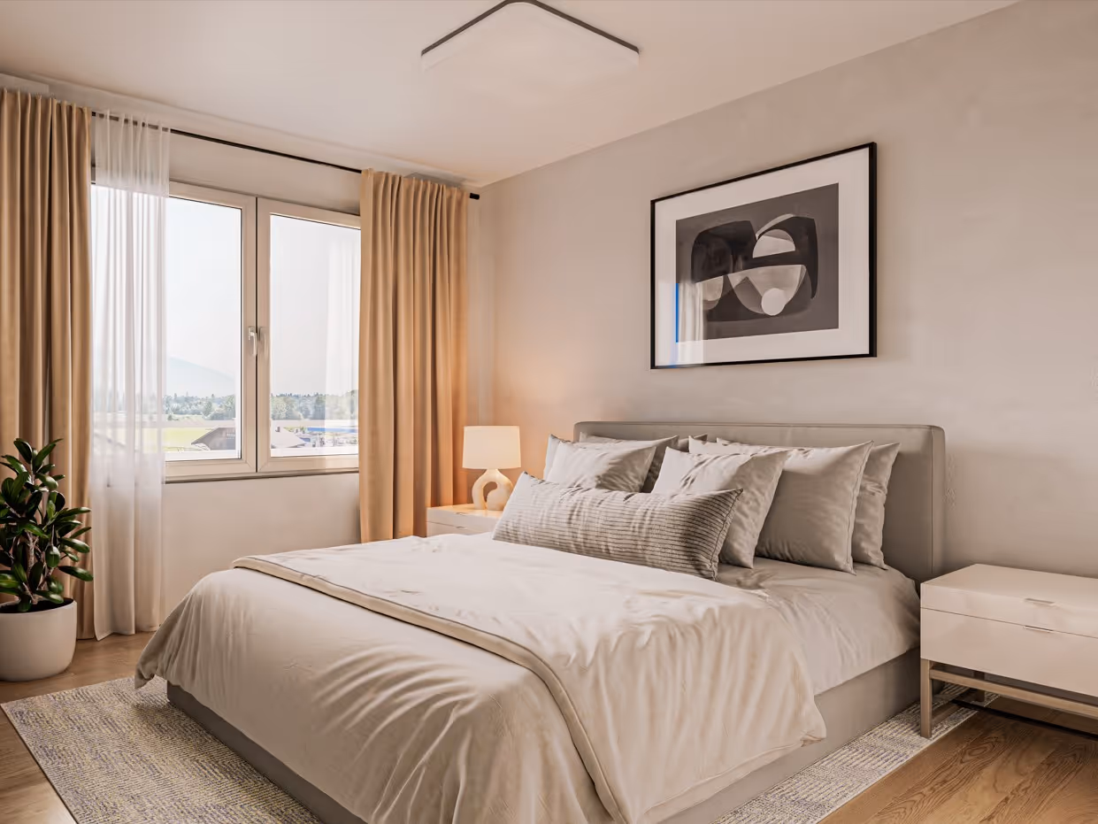 Hell eingerichtetes Schlafzimmer mit großem Bett, mehreren Kissen, Nachttisch mit Lampe und großem Fenster mit Vorhängen.