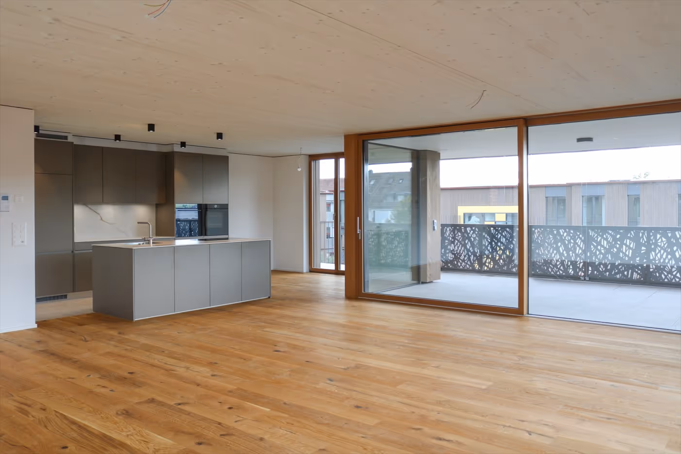 Moderner offener Küchenbereich mit grauer Kücheninsel, Holzboden und großen bodentiefen Fenstern zum Balkon.