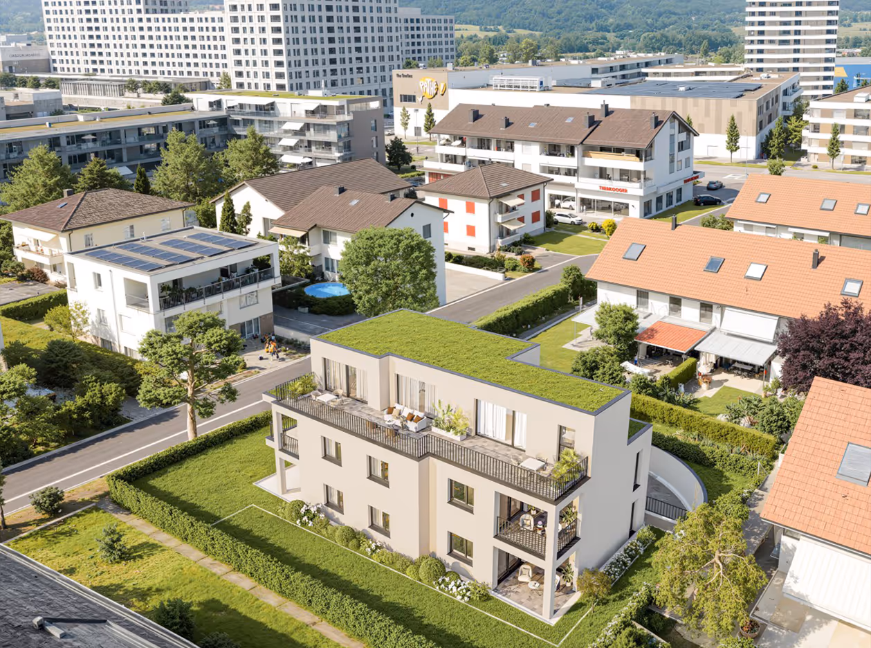 Luftaufnahme eines modernen Wohngebäudes mit begrüntem Dach in einem Wohnviertel mit mehreren Häusern und Bäumen.