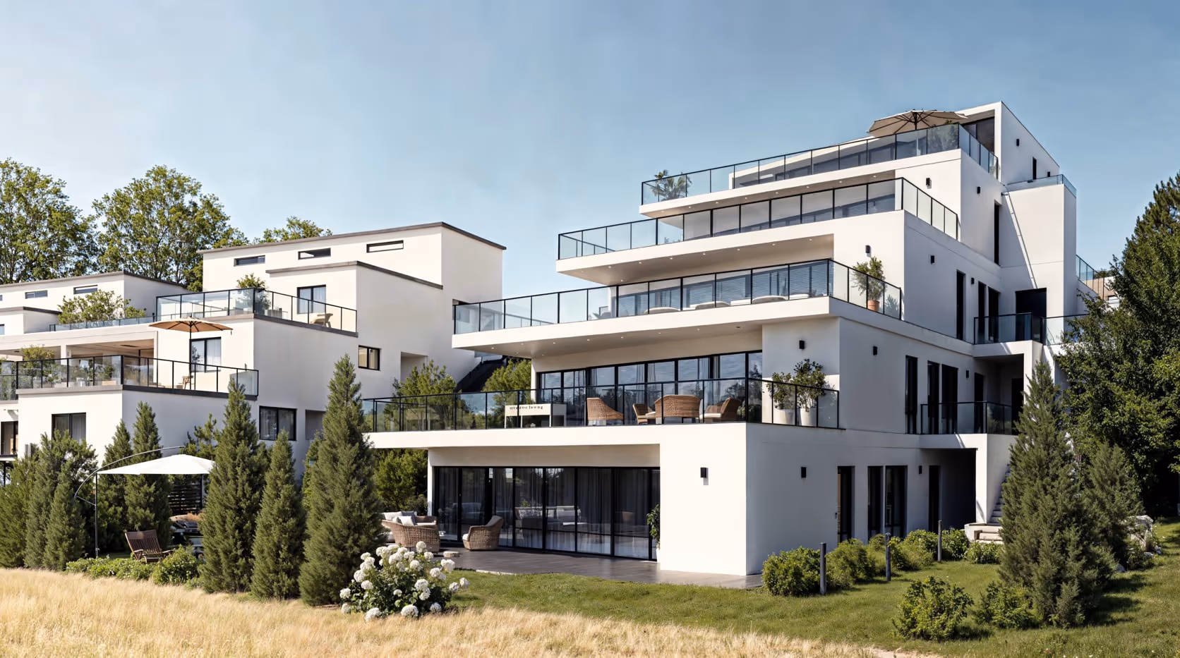 Moderne weiße mehrstöckige Wohngebäude mit großen Glasbalkonen, Terrasse und umgeben von Bäumen und Rasen.