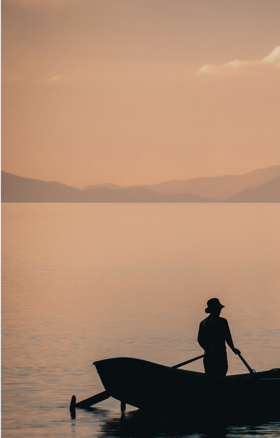 A silhouetted person in a small rowing boat at sunset