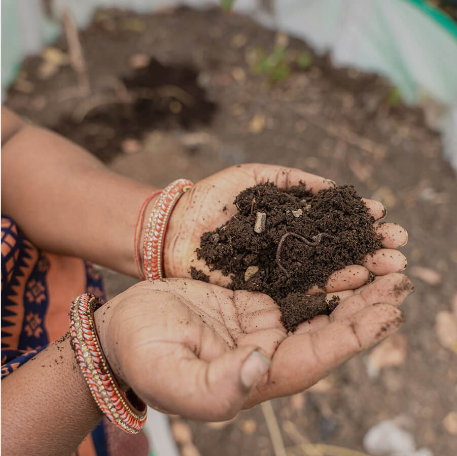 A close up shot of someone's hands holding some soil with a worm crawling through