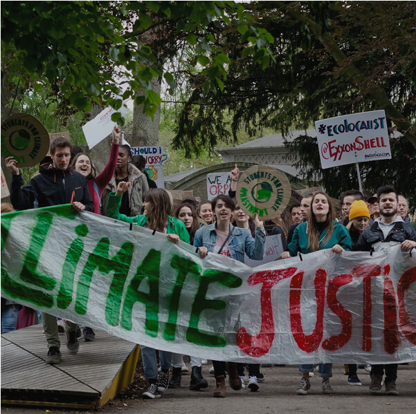 A group of people at a demonstration holding up a "Climate Justice" hand made sign