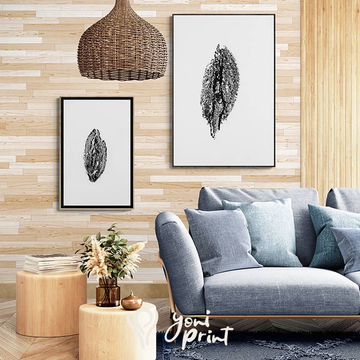 Two minimalist black-and-white yoni art prints hang on a light wood setting above a blue sofa.