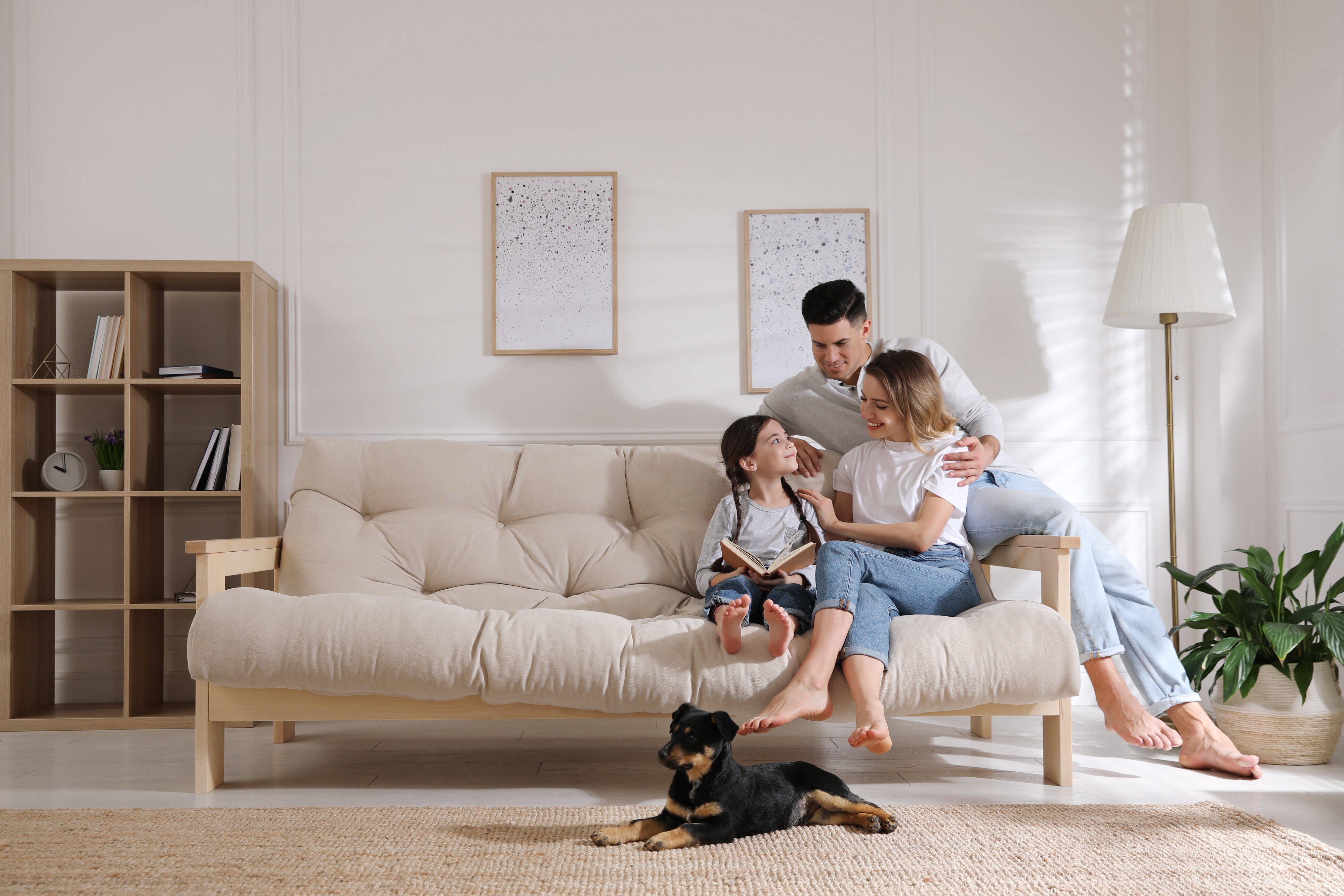 Happy family with a child reading on a sofa and a dog lying on the rug, depicting a comfortable and pet-friendly home life at Canvas at Gateway in Denver, CO.