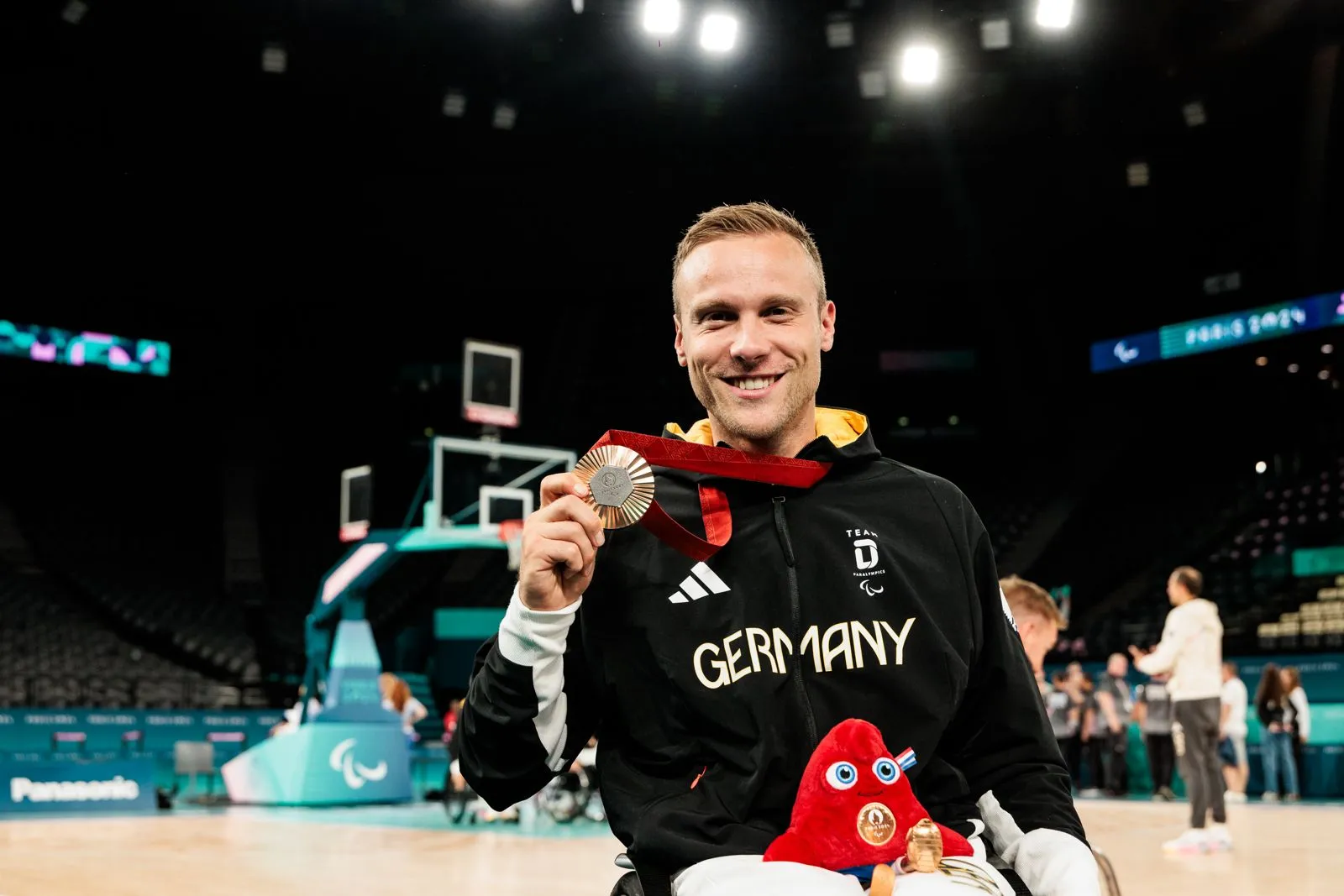 Rollstuhlbasketballer hält die Olympiamedaille in die Kamera und lächelt