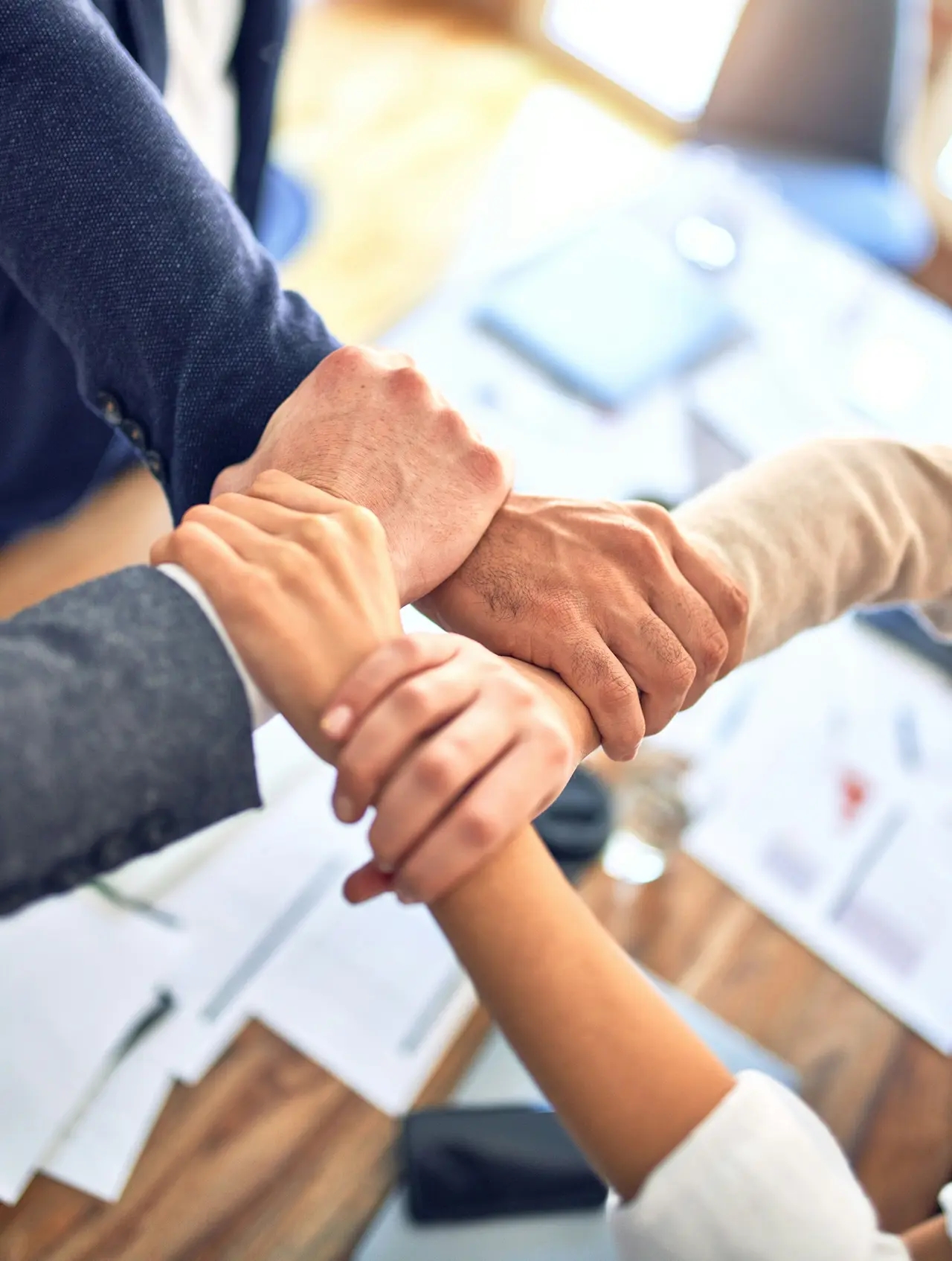 Business professionals joining hands over a table, symbolizing teamwork and collaboration in a meeting setting.