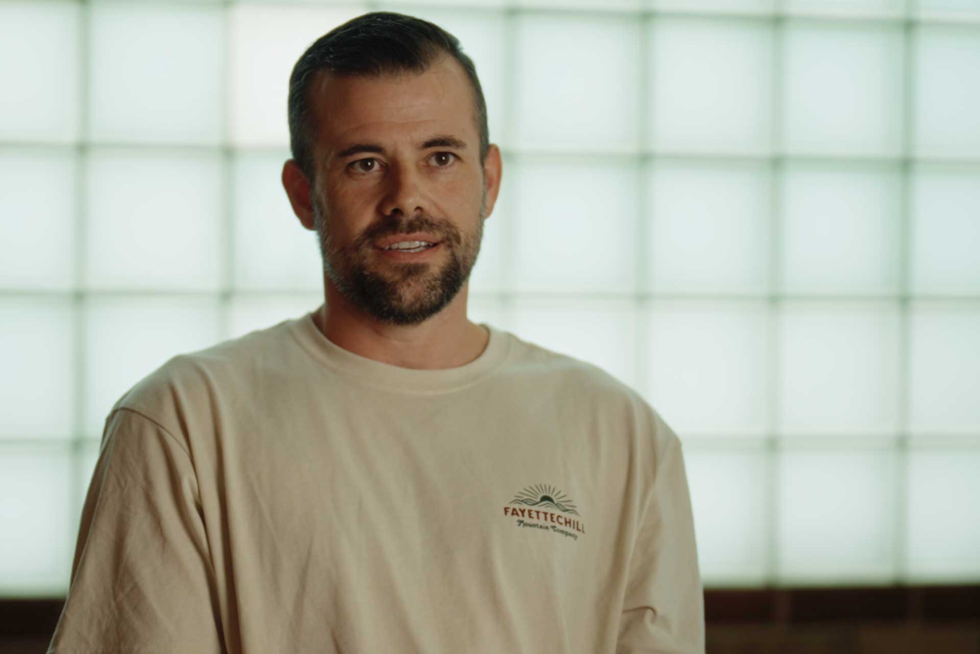 Man with short dark hair and beard wearing a beige Fayette Chill Mountain Company shirt.