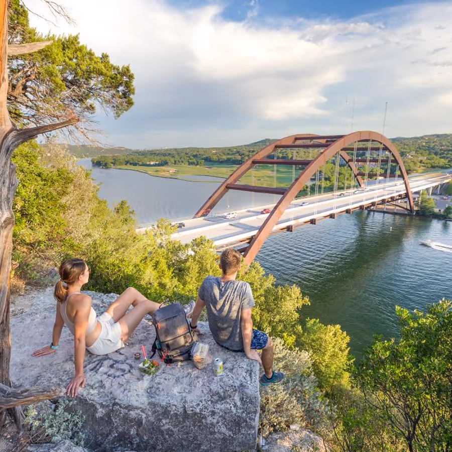 A woman and a man sit on a rock overlooking a bridge.