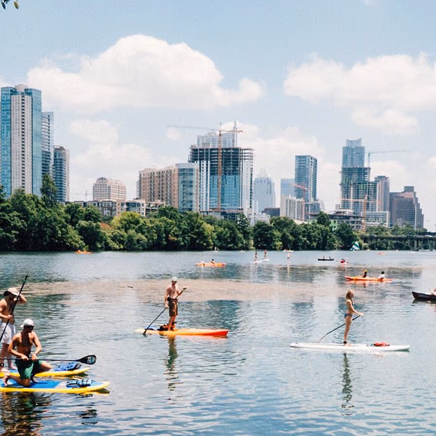 A group of people are paddling on the water in front of a city.