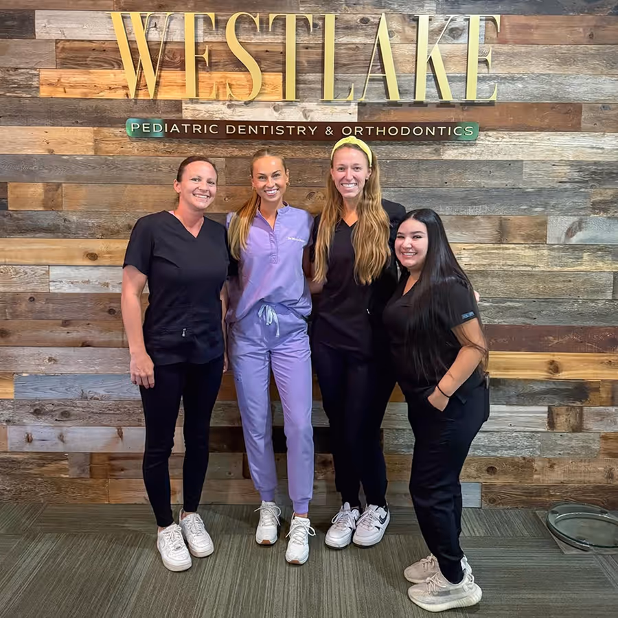 Four women in scrubs pose for a picture in front of a sign for Westlake Pediatric Dentistry.