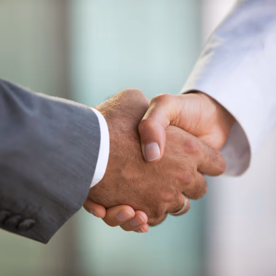 Two men shake hands in front of a window.